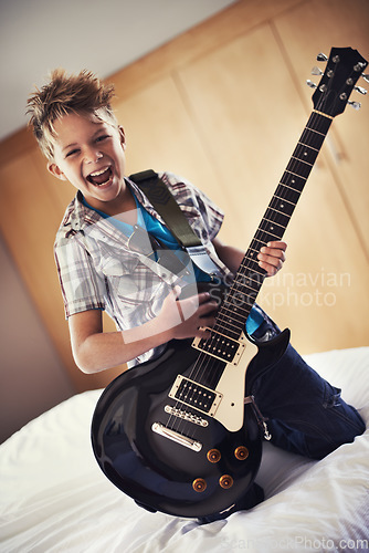 Image of Happy, portrait and child with guitar on bed for music lesson or practice at modern home. Fun, rockstar and young boy kid playing electric string instrument for concert in bedroom for hobby at house.