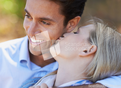 Image of Happy couple, closeup and kiss in nature for embrace, love or support in relax for outdoor bonding. Young woman kissing man on cheek with smile for affection, comfort or romance in forest together