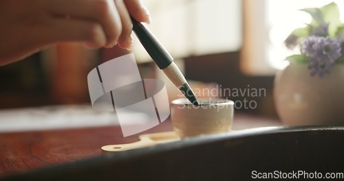 Image of Brush, closeup and hands at a table for calligraphy, writing or ancient Japanese art in a house. Letter, communication and zoom on person fingers with traditional ink stroke, penmanship or art tool
