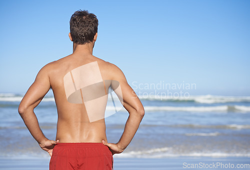 Image of Man, lifeguard and beach for security, emergency or outdoor swimming in health and safety. Rear view or back of male person or professional swimmer stranding ready for patrol at sea or ocean coast