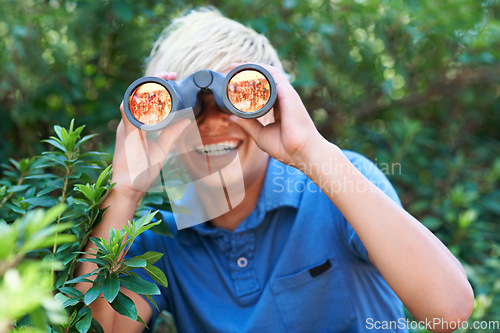 Image of Boy, child with binoculars and search in nature for learning and fun, forest and adventure at summer camp. Young camper, happy with leaves and explore environment outdoor for discovery and wildlife