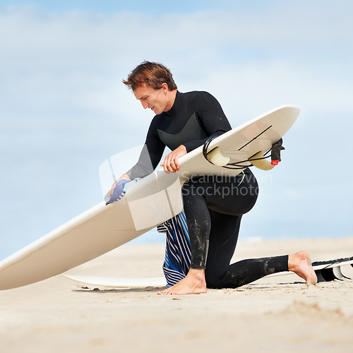 Image of Surfer, man and getting ready with surfboard on beach with wetsuit, blue sky and cleaning with mock up space. Rear view, athlete and person by ocean for training, surfing workout and extreme sports