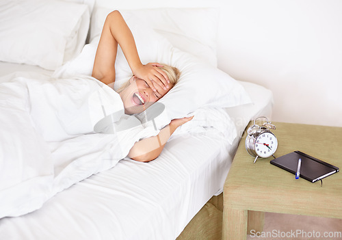 Image of Morning, alarm clock and yawn with woman waking up in bedroom of home for start of Monday. Headache, stress or fatigue and young blonde person sleeping in bed of apartment with ring for time