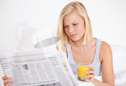 Image of Young woman, worry or orange juice with newspaper on bed, frustrated or drink for health body in wellness. Blonde model, headlines or glass of fruit smoothie to detox, morning or vitamin c in bedroom