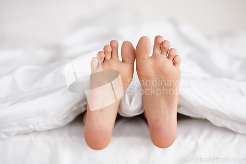Image of Bed, feet and person sleeping in home, relax and resting nap in sheets for health, calm and leisure in the morning. Foot, bedroom and closeup of toes in blankets, skin of legs and comfort in house