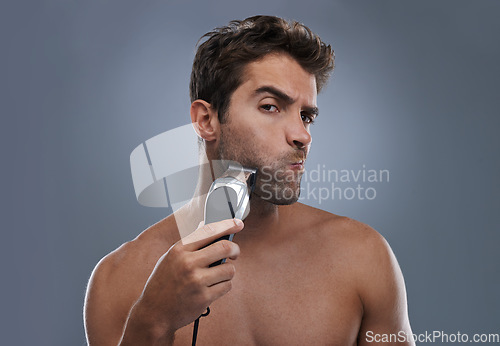 Image of Man, shaving and machine in studio for beard grooming, skincare and portrait by grey background. Person, model and self care for hygiene, facial hair removal and electric razor for cosmetic change