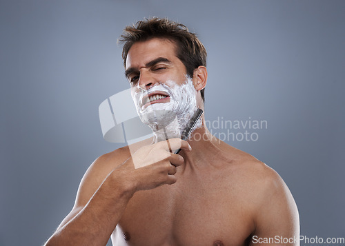 Image of Man, shaving and pain in studio portrait with grooming, skincare and wellness with stress by grey background. Person, model and anxiety with beard, facial hair removal and product for cosmetic change