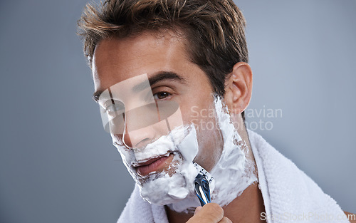 Image of Man, blade and shaving beard in studio closeup for grooming, skincare and portrait by grey background. Person, model and self care with cream, facial hair removal and product for cosmetic change