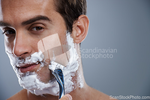 Image of Man, blade and shaving in studio portrait for wellness, skin or grooming with cream by grey background. Person, model and closeup with beard, facial hair removal and foam product for cosmetic change