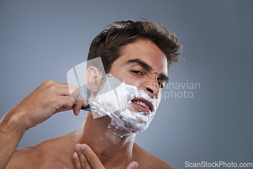 Image of Man, shaving and frustrated with razor in studio portrait for wellness, skin and grooming by grey background. Person, model and stress with beard, facial hair removal and product for cosmetic change