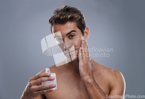 Image of Portrait, cream and man with skincare, wellness and beauty with lotion and moisture with glow and bottle on a grey studio background. Portrait, person and model with grooming routine and treatment