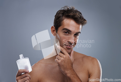 Image of Studio, portrait and model with aftershave for skincare, grooming and facial treatment or cologne. Man, face and happy for bottle for cosmetics product, fragrance and male beauty by gray background