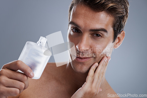 Image of Studio, portrait and man with aftershave for beauty, grooming and facial treatment or cologne. Model, face and happy with bottle for cosmetics product, fragrance and male skincare by gray background