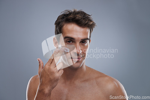 Image of Portrait, cream and man with skincare, shine and beauty with glow on grey studio background. Apply, person and model with morning routine or treatment with lotion or moisture with wellness or face