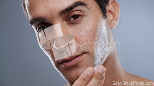 Image of Portrait, cream and man with dermatology, cosmetics and beauty on a grey studio background. Portrait, person and model with grooming routine or skincare with lotion or moisture after shave with shine