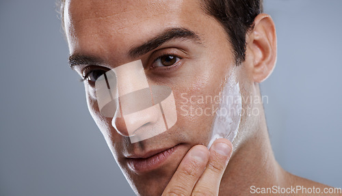 Image of Portrait, cream and man with skincare, dermatology or wellness on grey studio background. Portrait, person or model with grooming routine or treatment with lotion or moisture with glow or smooth skin