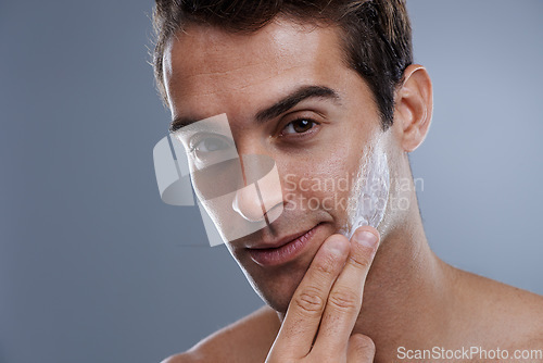 Image of Portrait, cream and man with skincare, glow and moisture on a grey studio background. Face, person and model with grooming routine and treatment with lotion and dermatology with wellness or shine