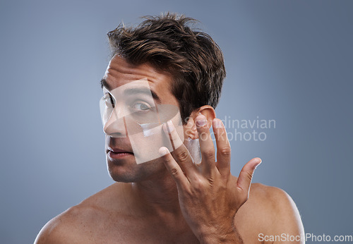 Image of Portrait, cream and man with skincare, cosmetics and beauty on a grey studio background. Portrait, person and model with grooming routine and treatment with lotion and moisture with wellness and glow