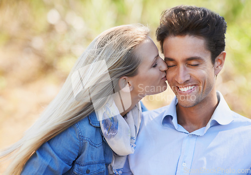 Image of Happy couple, kiss and cheek in nature for love, bonding or support in relax for outdoor affection. Face of young woman and man smile for embrace, intimacy or romance in forest or woods together
