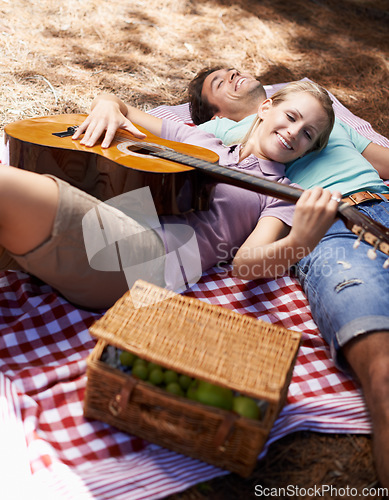 Image of Happy couple, picnic and playing guitar for love, romance or music in outdoor bonding, fun or relaxing together in nature. Man and woman smile with instrument for acoustic sound or songs outside