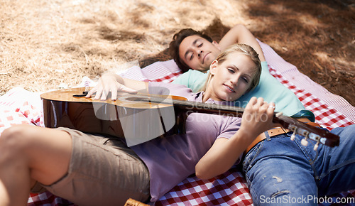 Image of Couple, picnic and playing guitar for romance, music or love in outdoor bonding, fun or relaxing together in nature. Young man and woman smile with instrument for acoustic sound or songs outside