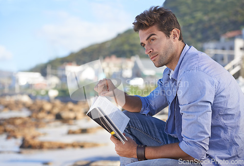 Image of Beach, book and young man reading for knowledge or relaxing hobby on vacation or holiday. Travel, outdoor and handsome confident male person enjoying story or novel on weekend trip or adventure.