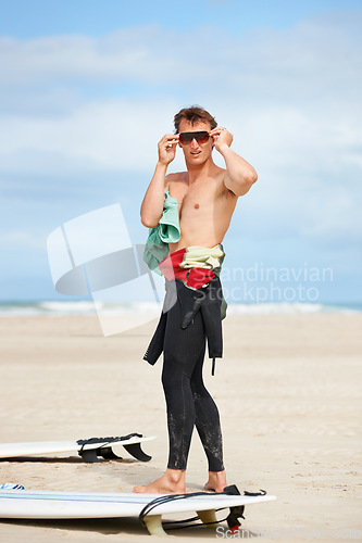 Image of Surfing, man and getting ready with sunglasses on beach with wetsuit, blue sky or surfboard with mock up space. Extreme sports, athlete and person by ocean for training, surfer workout or confidence