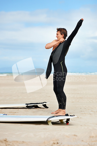 Image of Surfer, man and getting ready with surfboard by ocean with wetsuit, blue sky and dressing with mock up space. Extreme sports, athlete and person on beach for training, surfing workout and adventure