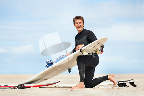 Image of Surfer, man and portrait with surfboard on beach with wetsuit, blue sky and cleaning with mock up space. Extreme sports, athlete and person by ocean for training, surfing workout and towel with smile