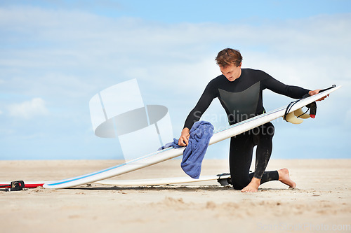 Image of Surfing, man and getting ready with surfboard on beach with wetsuit, blue sky and cleaning with mock up space. Extreme sports, athlete and person by ocean for training, surfer workout and towel