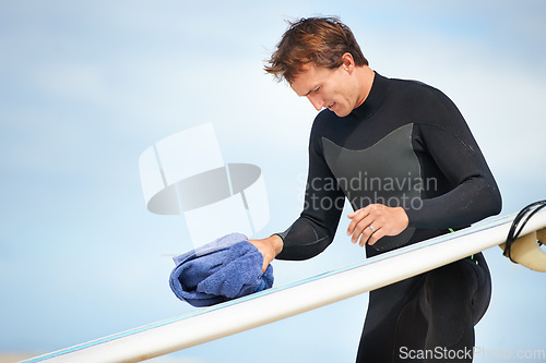 Image of Surfer, man and getting ready with surfboard on beach with wetsuit, blue sky and cleaning with mock up space. Extreme sports, athlete and person by ocean for training, surfing workout and towel