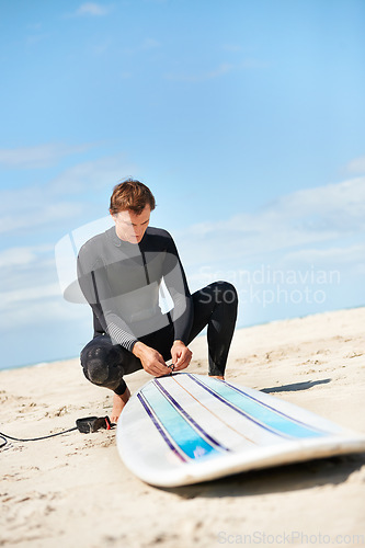 Image of Beach, man and surfboard rope outdoor in summer for exercise, fitness and workout. Surfer, wetsuit and person with leash by ocean for safety preparation, water sports and travel on holiday by sea