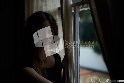 Image of Woman, portrait and relax by window at night in dark room in stress, anxiety or mental health and lonely at home. Young female person sitting by glass at house with insomnia in neighborhood apartment
