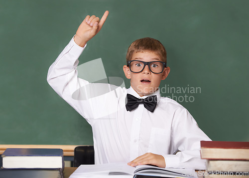 Image of Young boy, portrait and question at school for learning, education or interaction for knowledge by green chalk board. Face of male person, smart child or teenager with books and hand raised in class