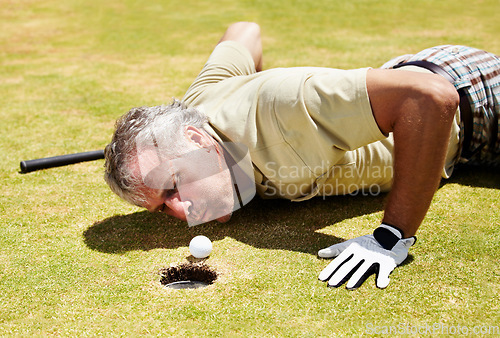 Image of Golf, man and blowing ball into hole on a grass field for player match and putting. Fitness, sport and funny mature male person playing on a lawn to blow golfer object into target space and cheating