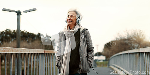 Image of Senior woman, headphones and music outdoor, walking and wellness with audio streaming and energy. Podcast, listen to radio and sound with female person on city bridge, exercise and travel with tech