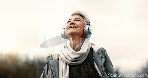 Image of Headphones, music and senior woman in nature for wellness, mental health and happy outdoor experience. Travel, listening and streaming service or podcast of elderly person thinking in park and winter