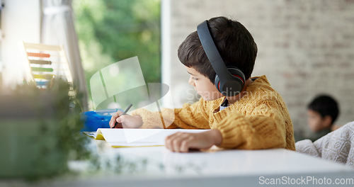 Image of Boy child, homework and writing with headphones, music and focus for learning, drawing or education. Young male kid, notebook and study with audio streaming, radio or listening online in family house