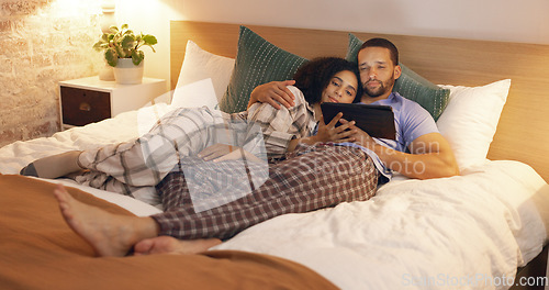 Image of Couple, happy and relax in bedroom with tablet at night, streaming movie and hug. Smile, technology and man and woman in bed on social media app, watching online video and bonding together in home.