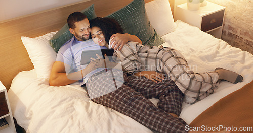 Image of Couple, happy and hug in bedroom with tablet at night, streaming movie and relax. Smile, technology and man and woman in bed on social media app, watching online video and bonding together in home.