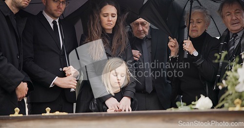 Image of Loss, grief and people at funeral with umbrella, flowers and coffin, family with sad child at service in graveyard. Roses, death and group in rain at casket in cemetery with kid at grave for burial.
