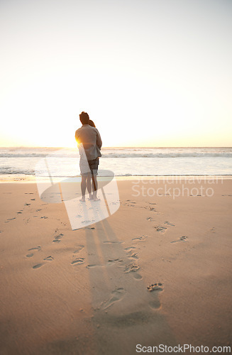 Image of Man, woman and beach love at sunset for romantic summer travel or adventure, bonding or marriage. Couple, footprints and embrace at water for dating tourism or nature vacation, environment or holiday