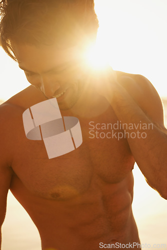 Image of Man, shirtless and happy on beach at sunset, confidence and tourist at sea on summer holiday. Male person, lens flare and outdoor adventure for fun, calming ocean and peaceful environment in nature