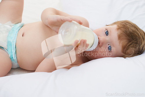 Image of Portrait, bottle and baby in bed drinking milk for meal, feeding or food lying down in home. Hungry child, wellness and healthy boy toddler with formula for nutrition, natural diet or growth alone