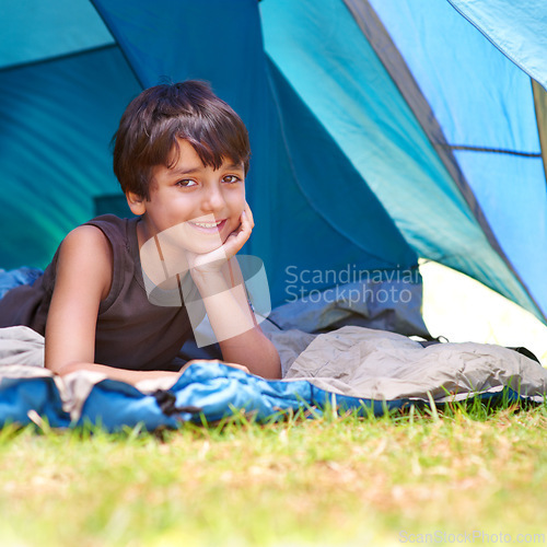 Image of Boy, child and camping, relax in tent and summer vacation with travel and happy in portrait outdoor. Rest on sleeping bag, young camper with smile and adventure in nature, childhood and recreation