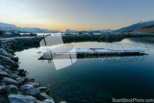 Image of A tranquil scene as the sun sets behind snow-covered mountains, reflecting off the placid sea.