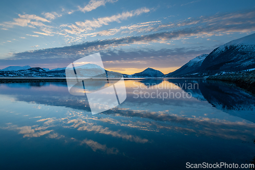 Image of Sunset colors paint the sky as the calm lake mirrors the mountains and clouds at dusk.