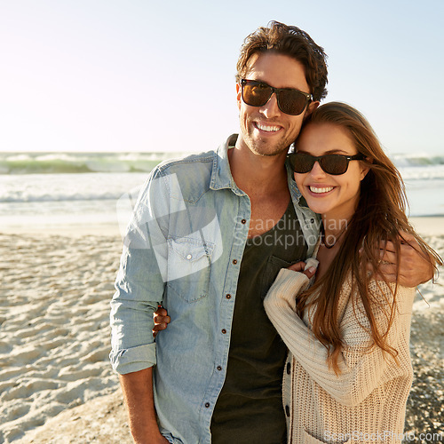 Image of Couple, beach and sunglasses with hug, happy or care with fashion, eye protection or vacation in summer. Man, woman and embrace with glasses for sun, trendy style or love by waves on tropical holiday