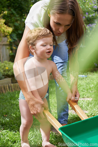 Image of Mother, boy and toddler with a wheelbarrow in garden, nature or grass for playing and fun in summer. Walking, backyard or kid with family, child development and mom with smile, growth and happiness