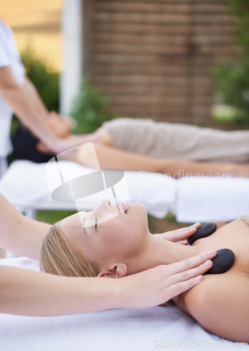 Image of Women, health and massage with hot stones, wellness and peace with hands for shoulder at spa. People, comfort and zen for physical therapy by masseuse, body treatment and detox on bed at resort